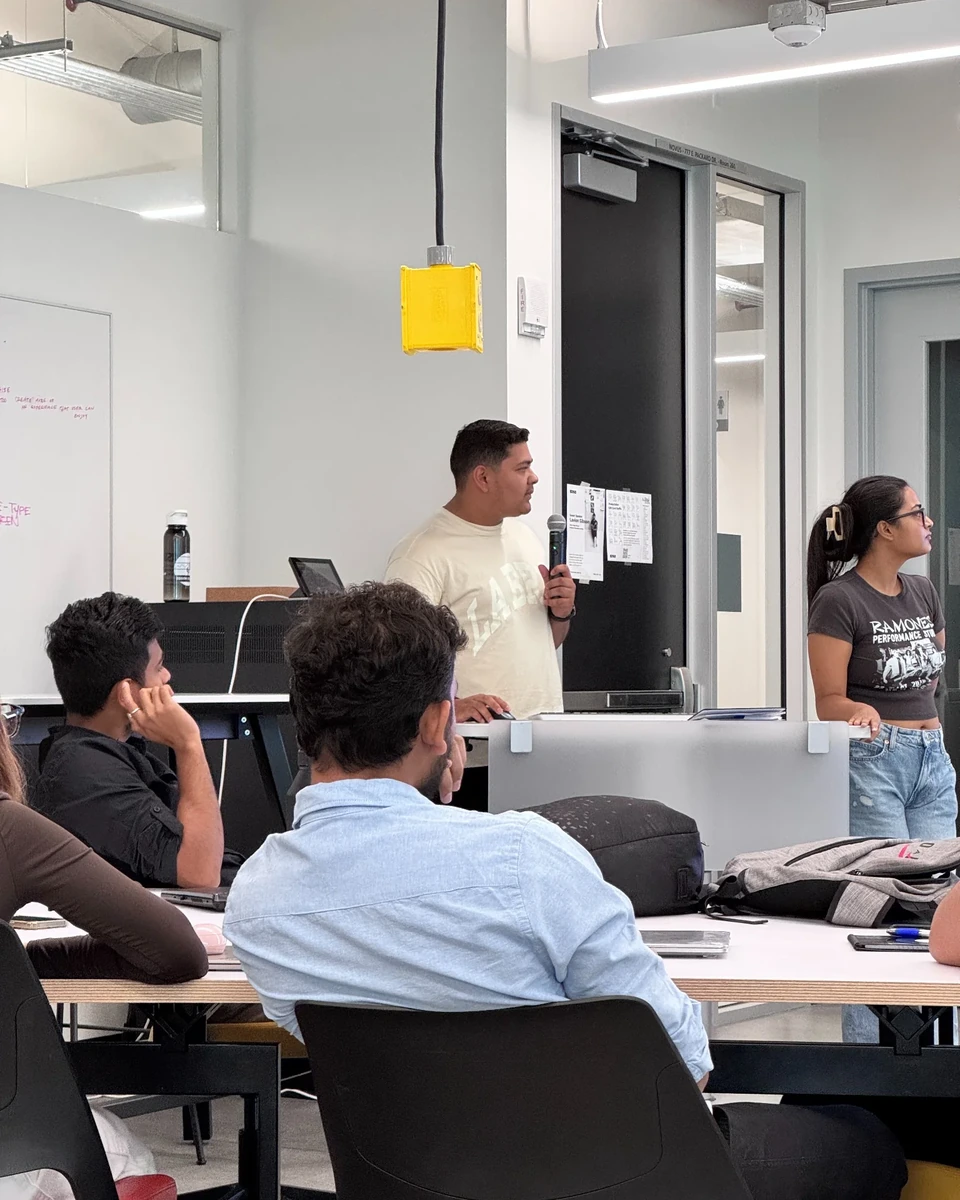 Prakhar Jain presenting in a critique room with audience members and the surrounding room context visible.