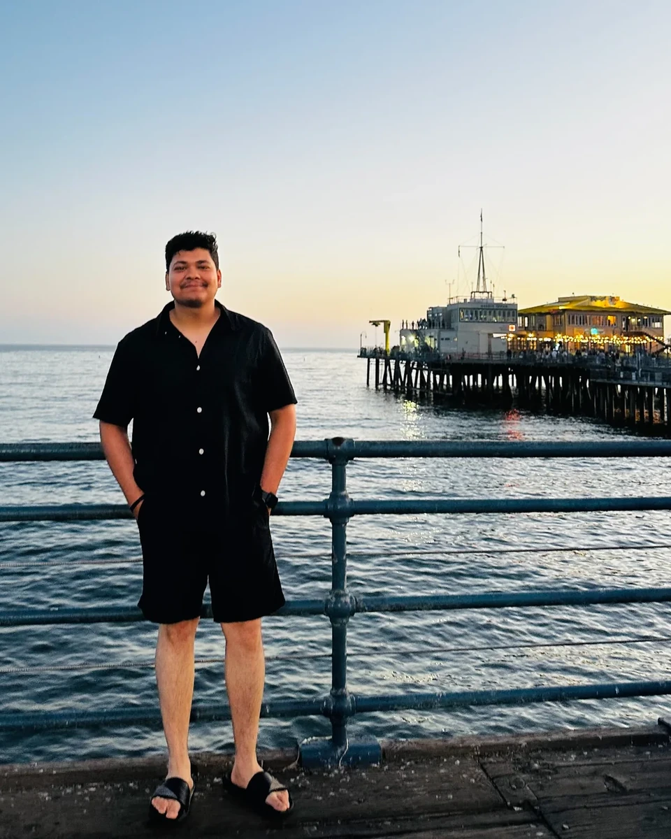 Prakhar Jain standing near the water with the Santa Monica pier and coastline visible behind him.