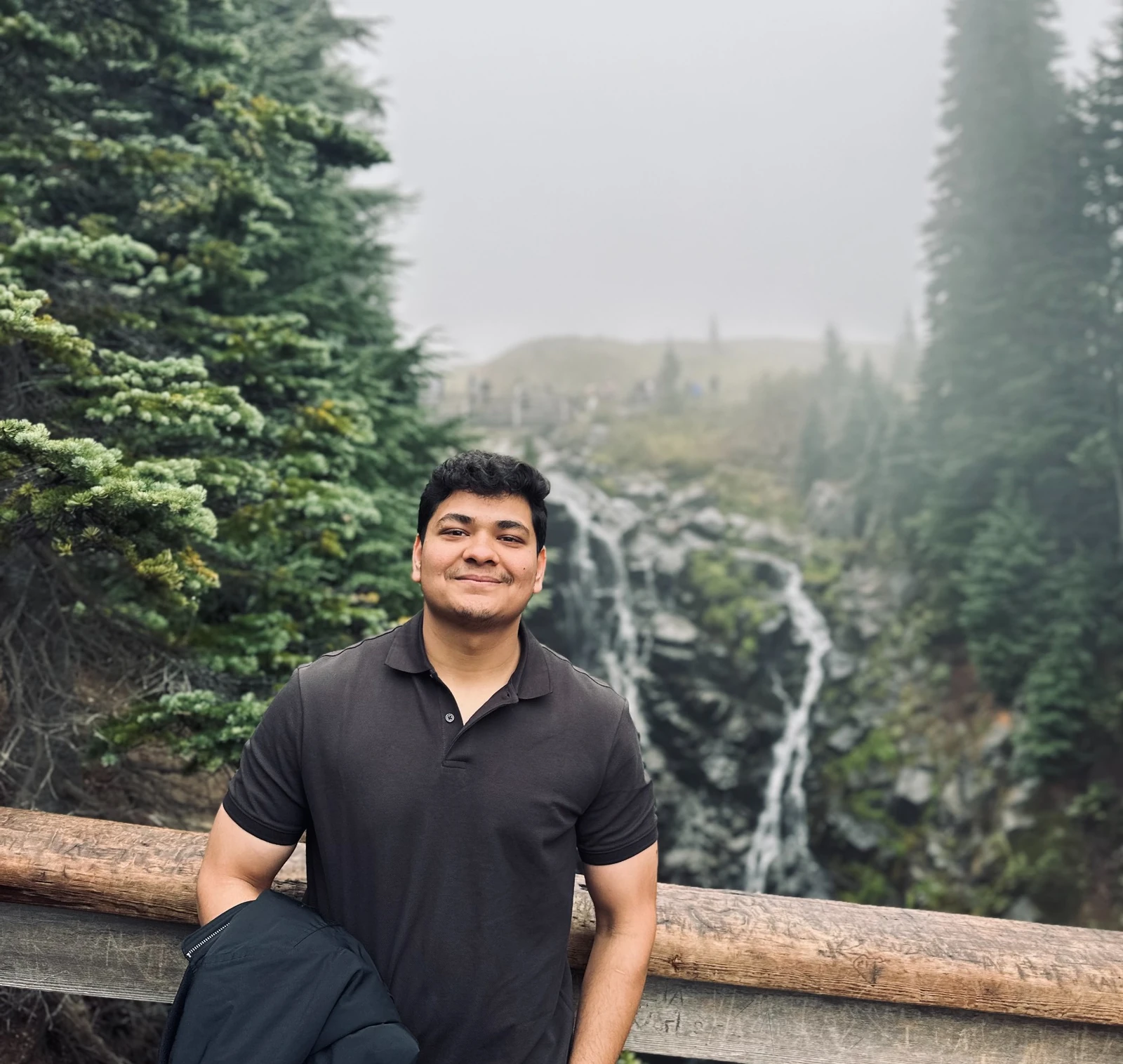 Prakhar Jain standing in front of a waterfall and evergreen forest.
