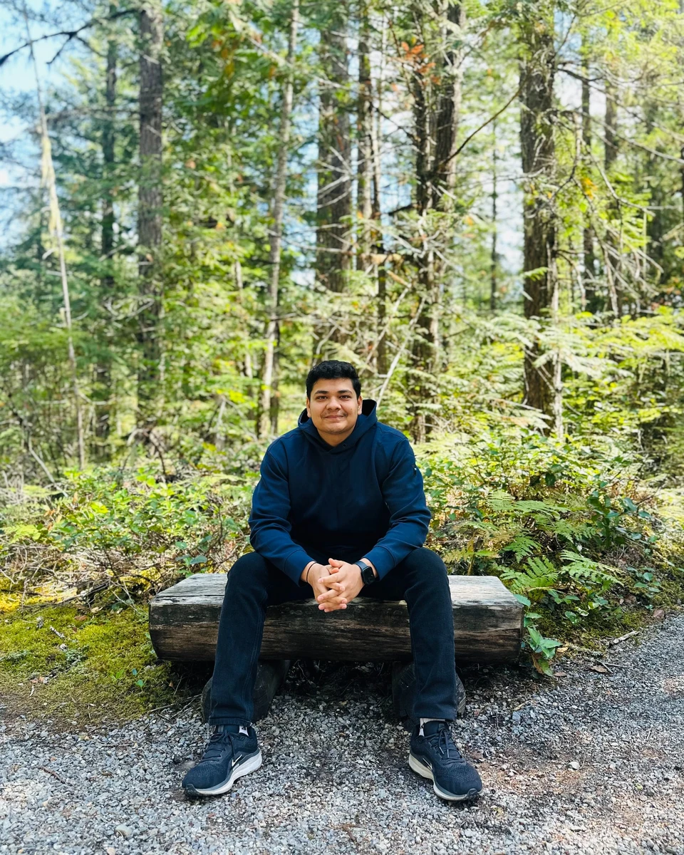 Prakhar Jain seated on a log in a forest with his hands clasped.