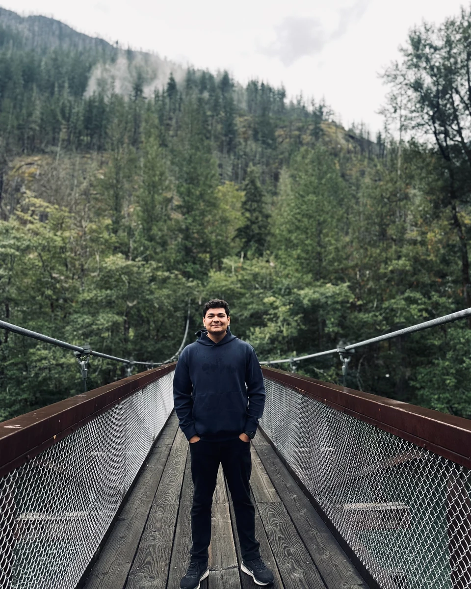 Prakhar Jain standing centered on a suspension bridge framed by forest.